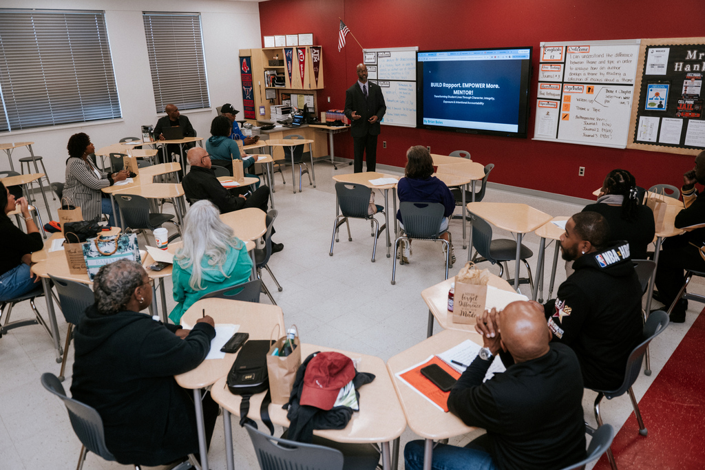AACPS Mentoring Conference 2026: A group of people sit in a circle in a classroom, listening to a person at the front.