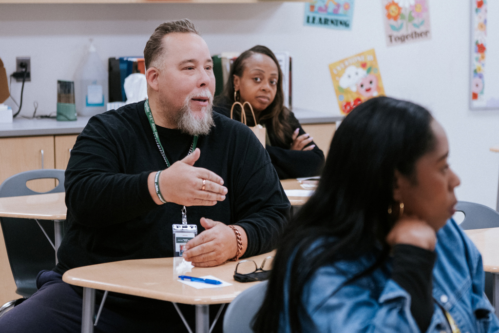 AACPS Mentoring Conference 2026: Three adults in a classroom setting, one speaking while another two listen, with a white board in the background.