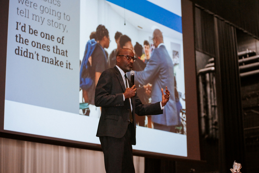 AACPS Mentoring Conference 2026: Superintendent Dr. Mark Bedell giving a speech with a screen behind them displaying an image of people in conversation.
