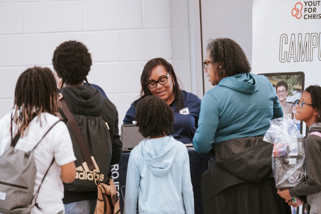 AACPS Mentoring Conference 2026: People gather at an event; a woman in glasses stands at a table with a laptop, facing a group.