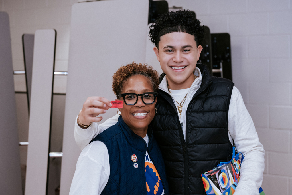 AACPS Mentoring Conference 2026: Two individuals smiling and posing with a red card, one wearing glasses and a vest, the other in a white shirt and vest.