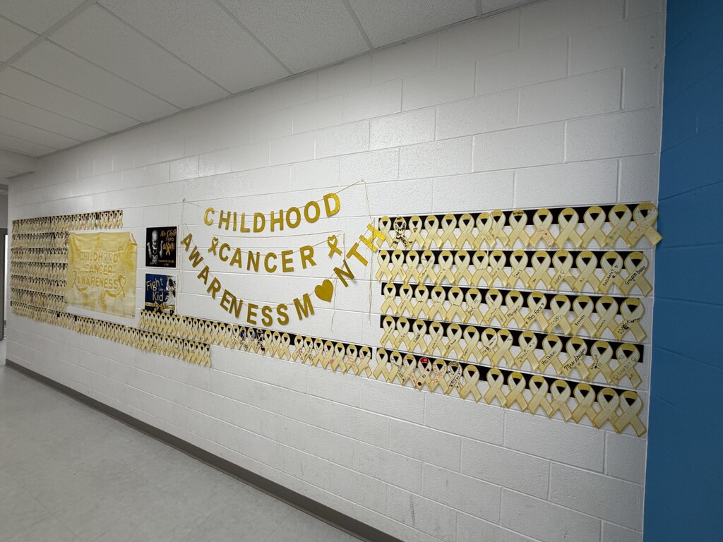 Hallway with white walls. A banner says "Childhood Cancer Awareness Month" with a heart symbol.