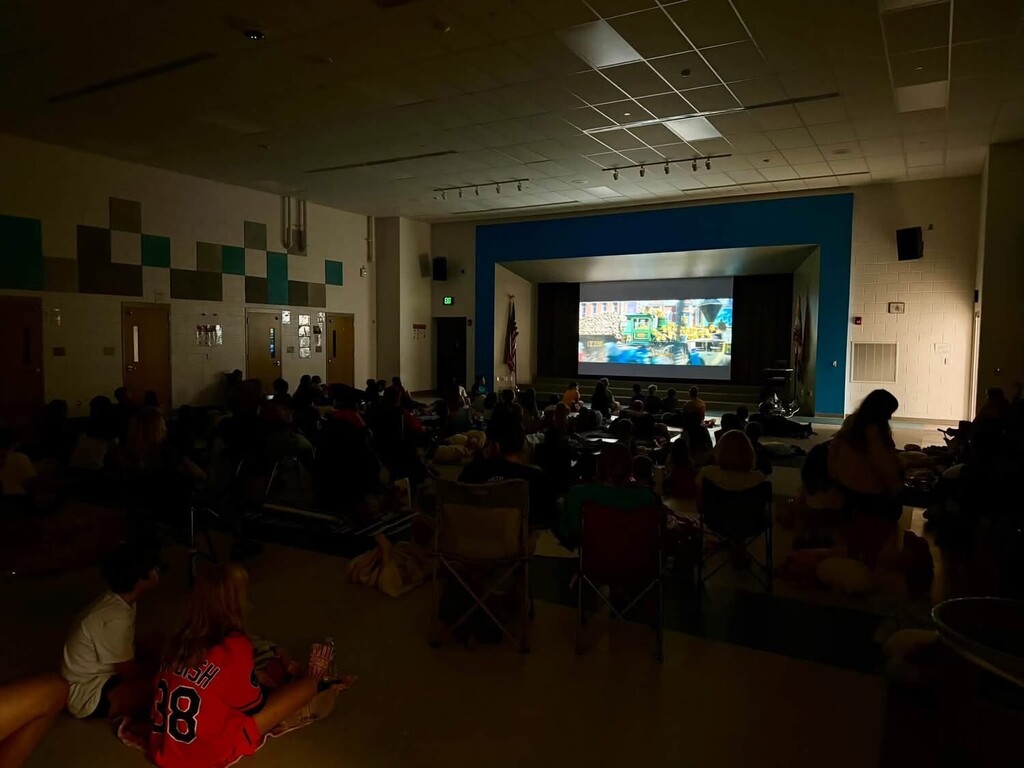Auditorium with people sitting in chairs watching a film on a large screen, walls with colorful patterns.