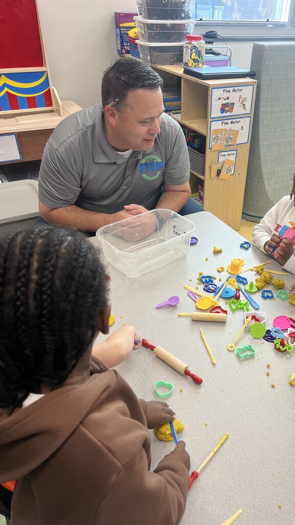 A man sits with two children at a table filled with colorful toys and tools.