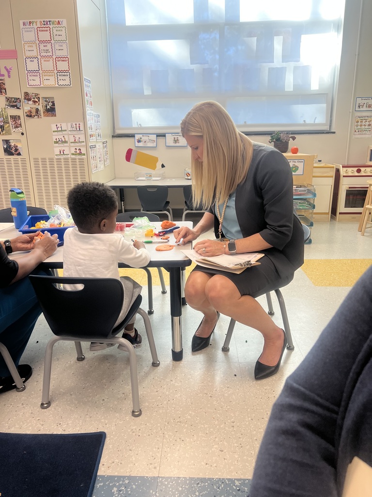 A woman and a young child seated at a table, the woman holding a clipboard and marker