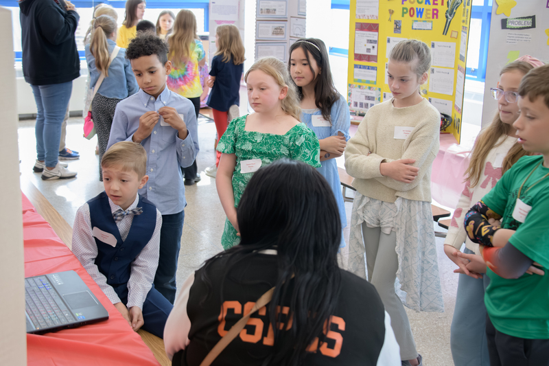 Students gather to around a science project to learn more about what a fellow student researched for their project