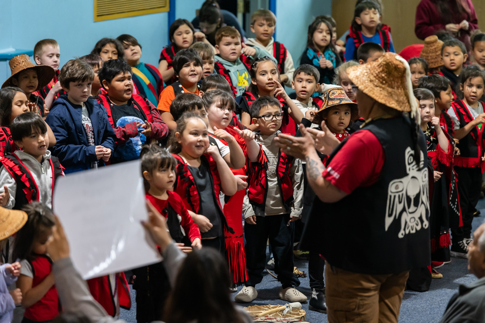 students in regalia singing with a man in front directing them