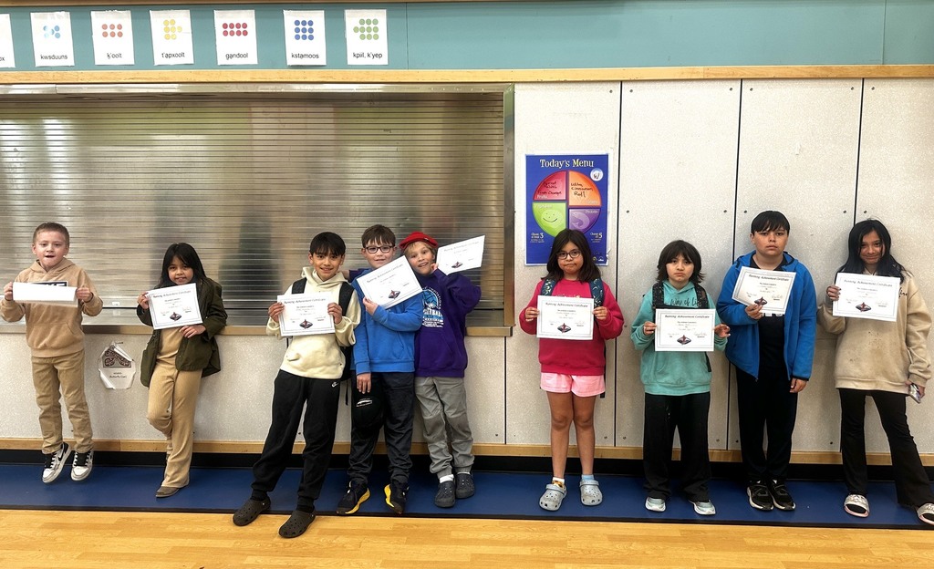 students standing in gym holding certificates.  They are wearing backpacks and smiling.