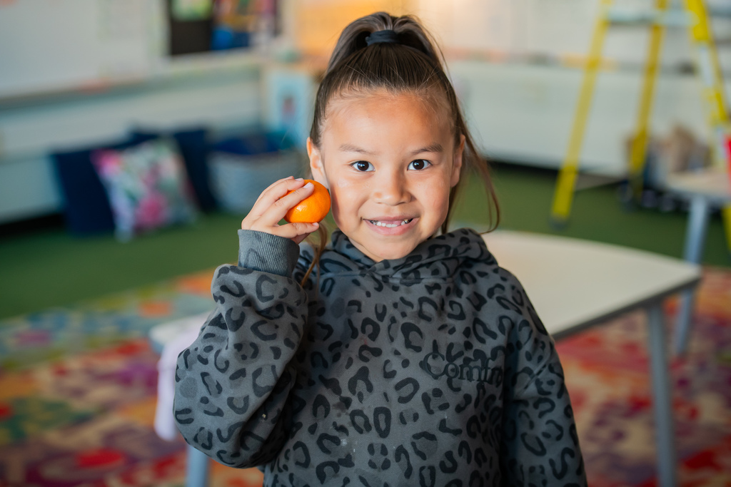 student holding a tangerine in a classroom