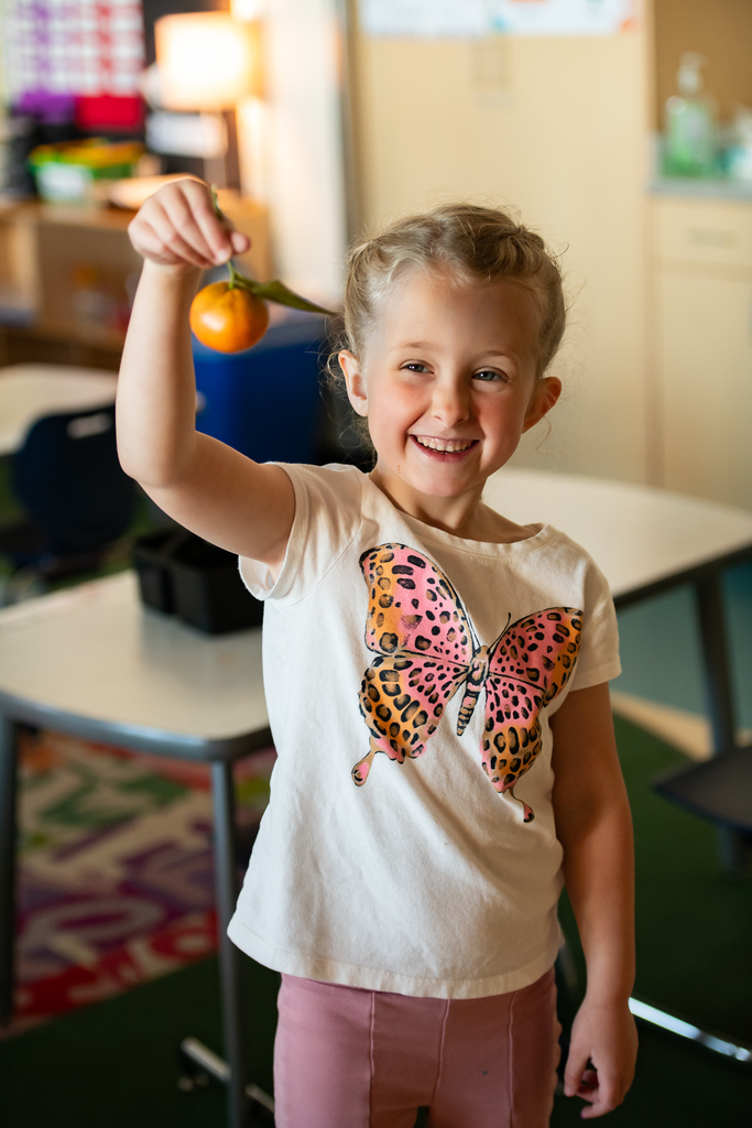 student holding a tangerine in a classroom