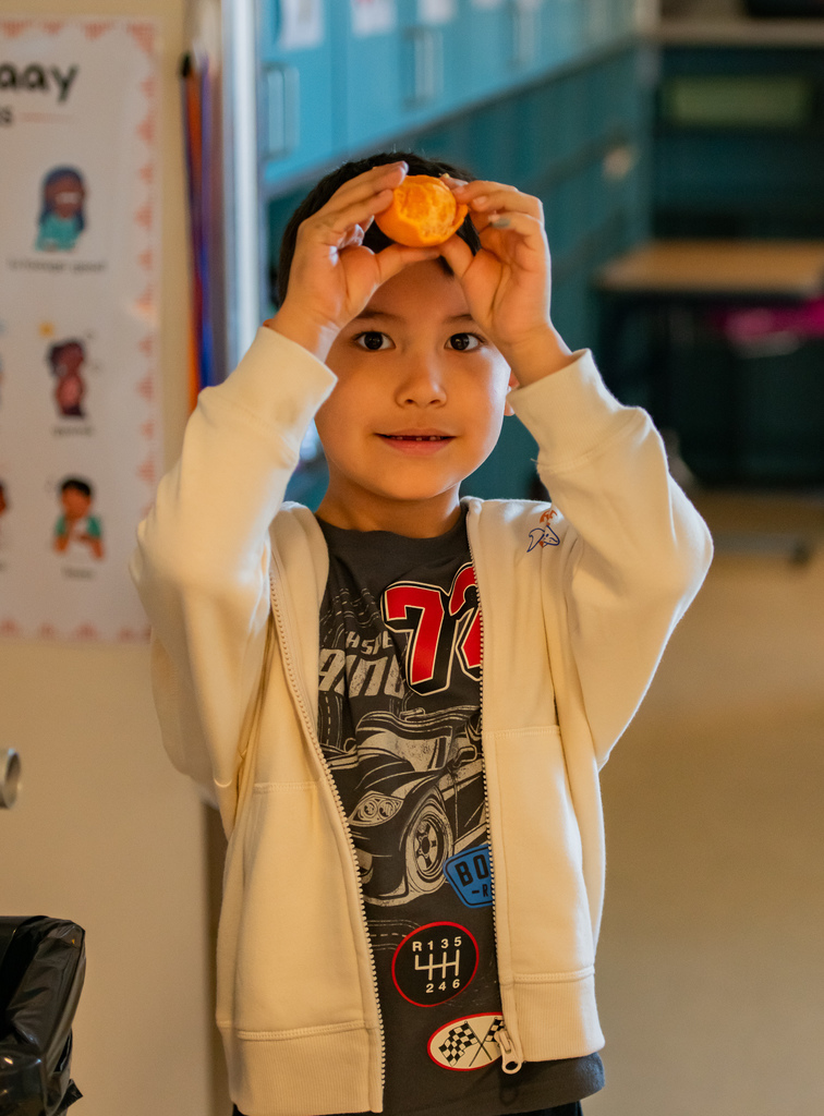 student holding a tangerine in a classroom