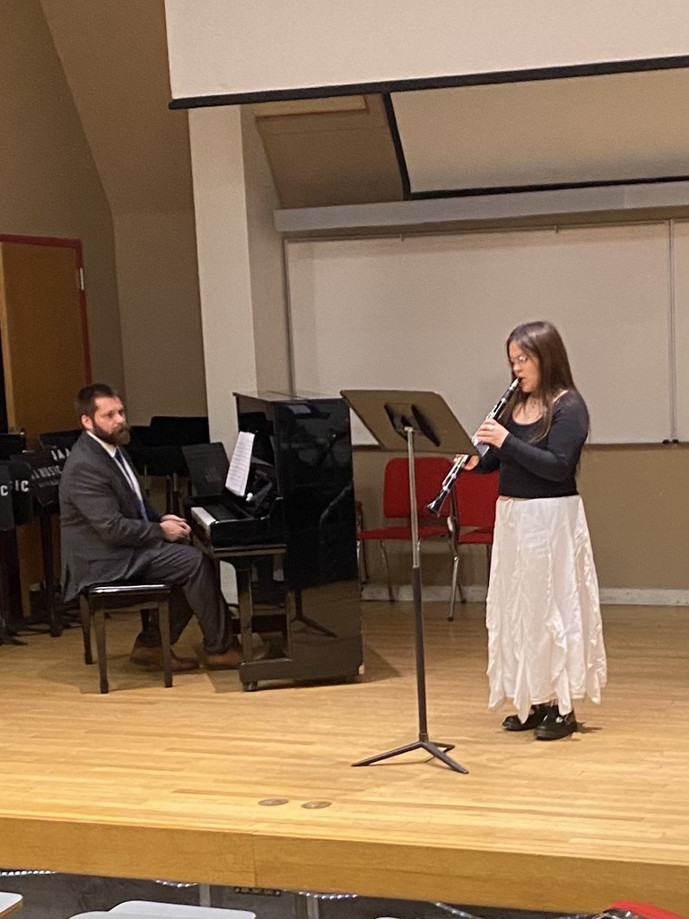 woman on stage playing clarinet, man playing piano with her