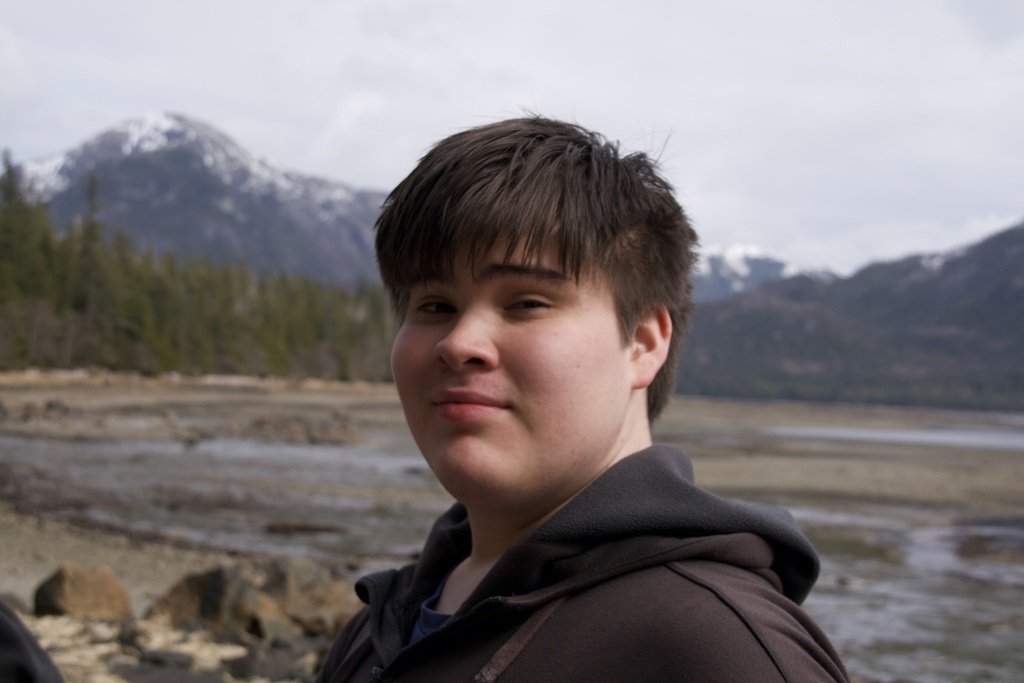 student smiling with mountains and a beach behind him