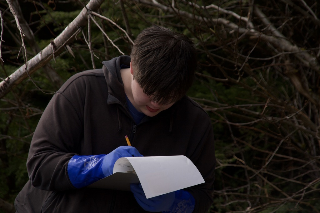 student writing on a clipboard in the woods