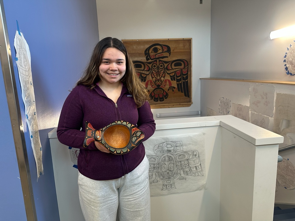 student holding carved halibut bowl with formline drawings around her