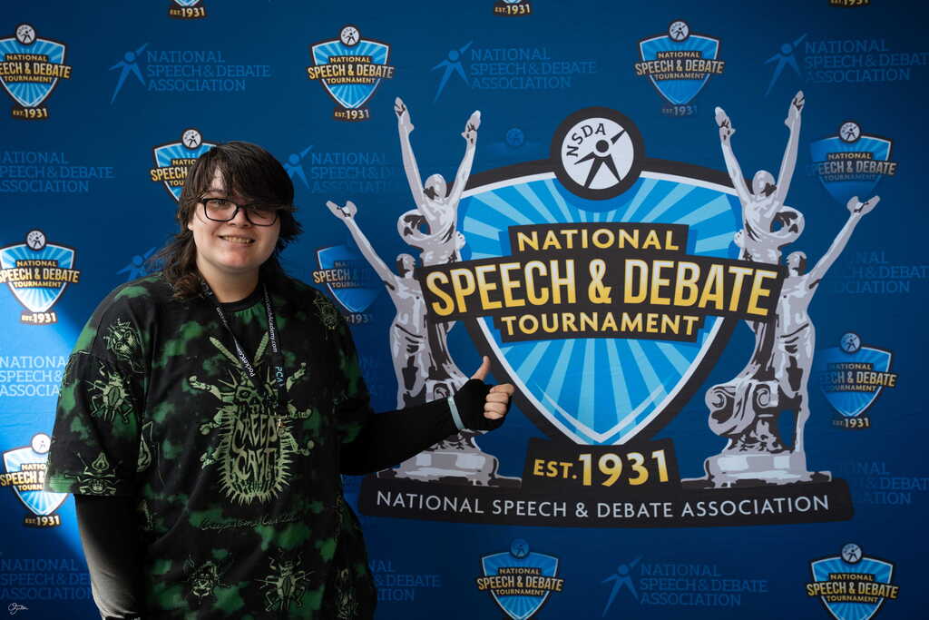 student in front of national speech and debate tournament sign,