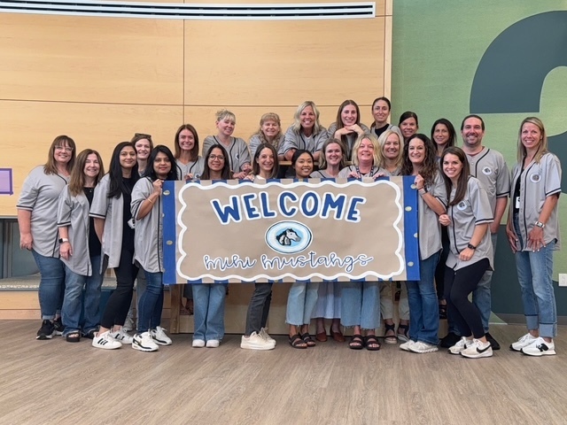 Team of teachers standing by a welcome sign.