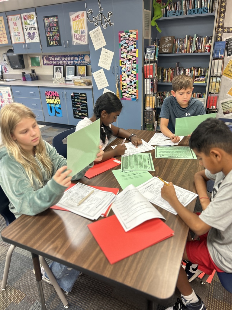 Students sitting at a table reading information or writing in a packet.