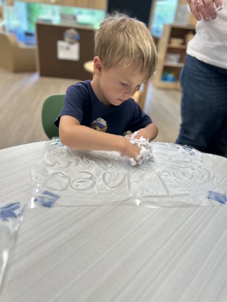 Student writing at the table with shaving cream.