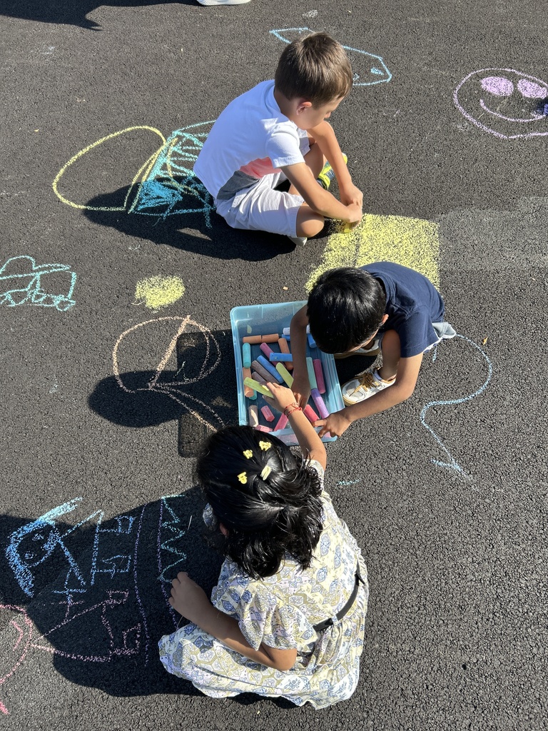 Students coloring with chalk on the blacktop.