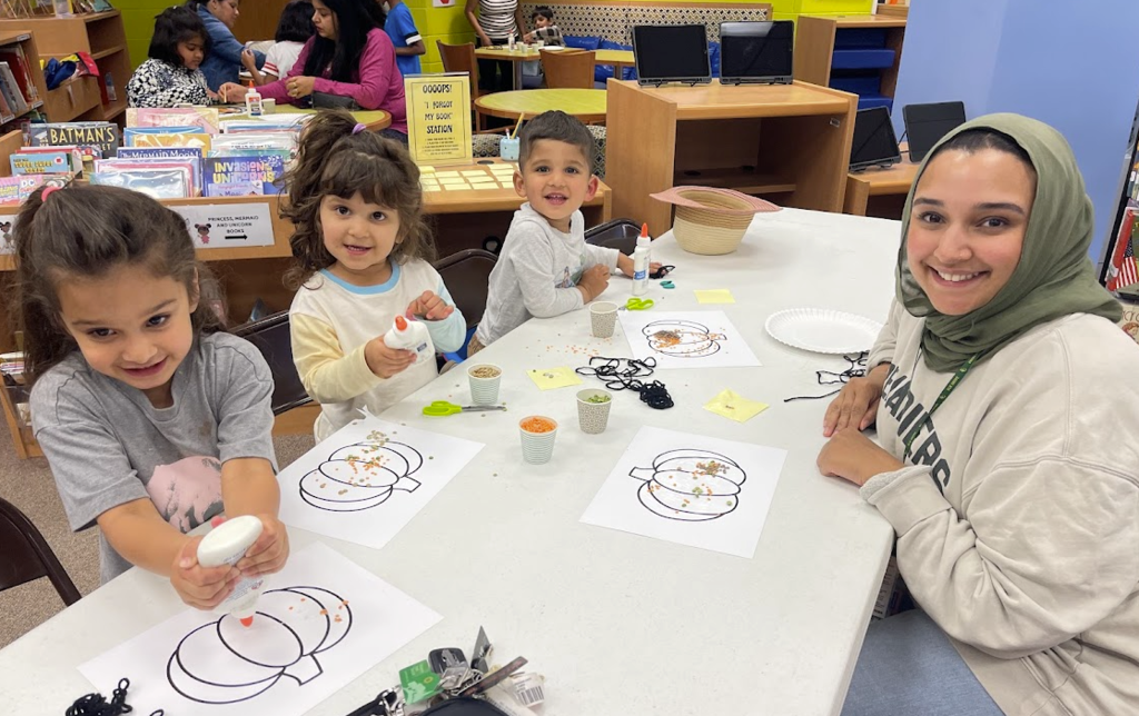 Mom witting at a table with her 2 kids making a craft.