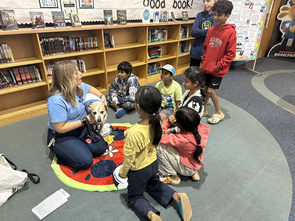 Students gathering on the ground with a therapy dog and a teacher.