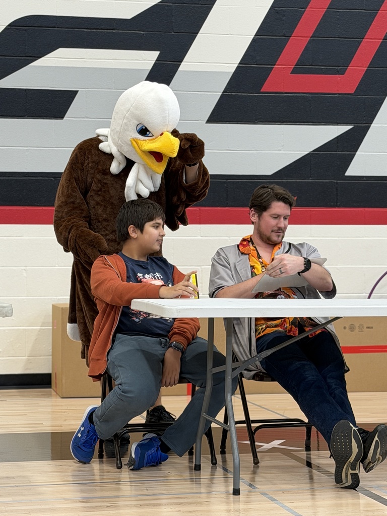 The eagle mascot is watching over the shoulder of a staff and student at a game.