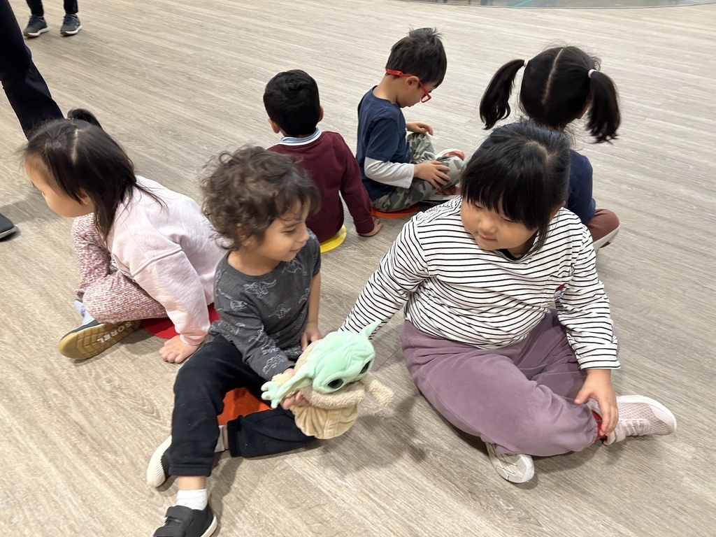 Students sitting in a circle passing a stuffed animal.