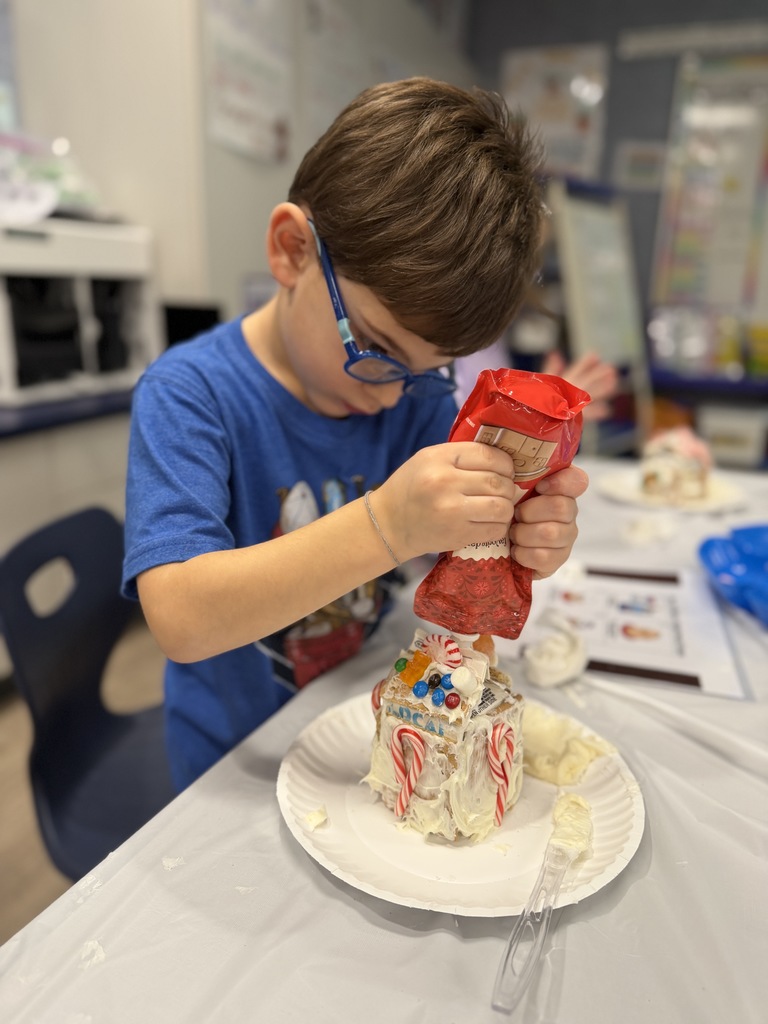STudent decorating their gingerbread house with frosting in his hand.