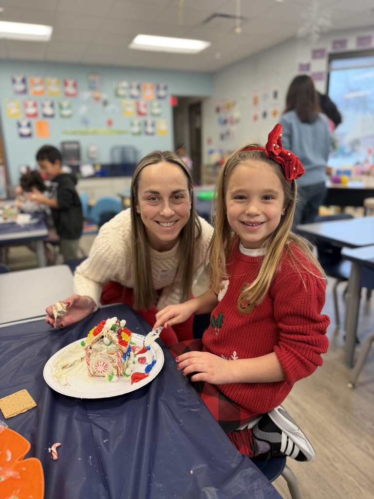 Mom and daughter standing together decorating their gingerbread house.