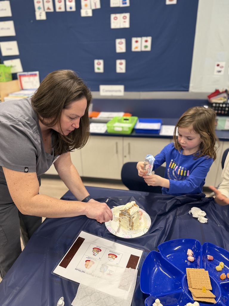 Mom bending over and helping her daughter with the frosting on the house.