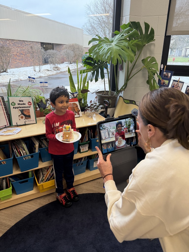Teacher taking a photo of a student holding his gingerbread house.