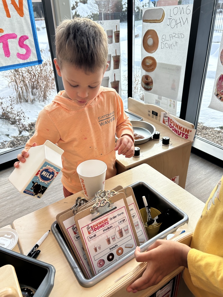 Student playing at play kitchen pouring a pretend drink.