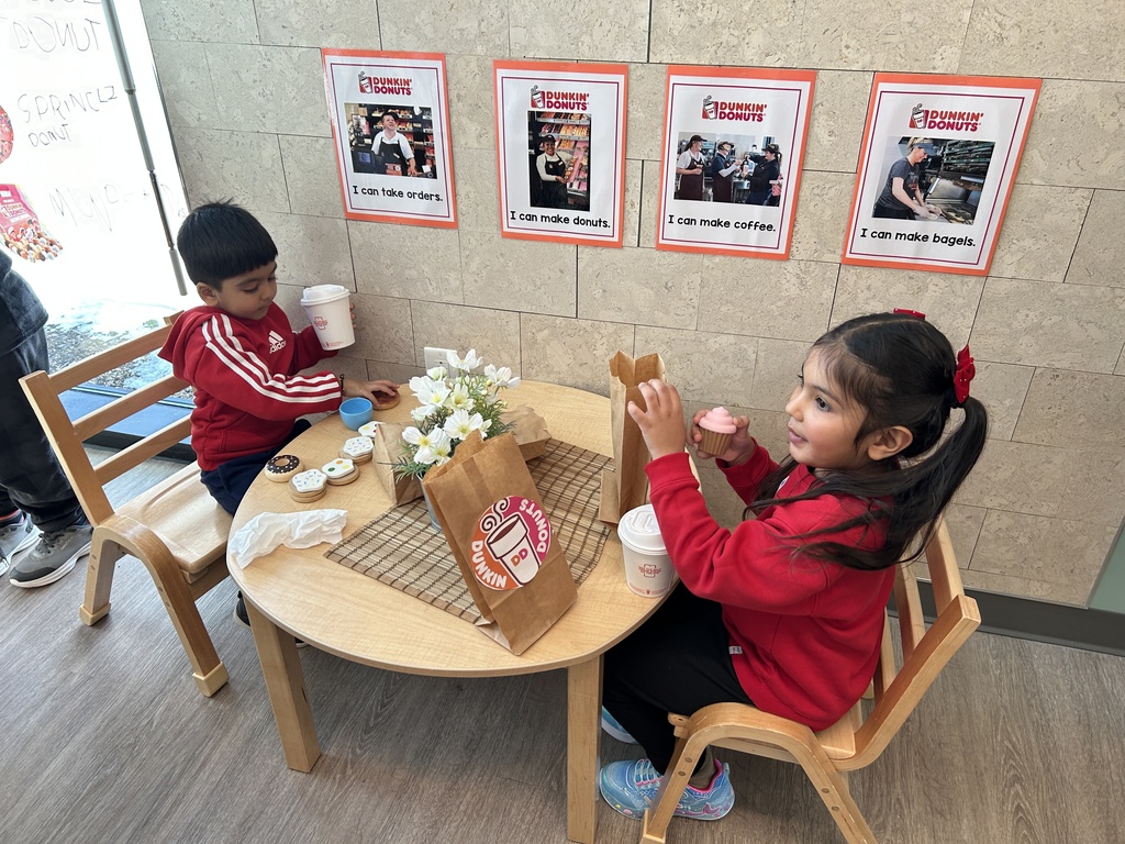 Two students sitting at a kids table pretending to eat Dunkin Donuts.