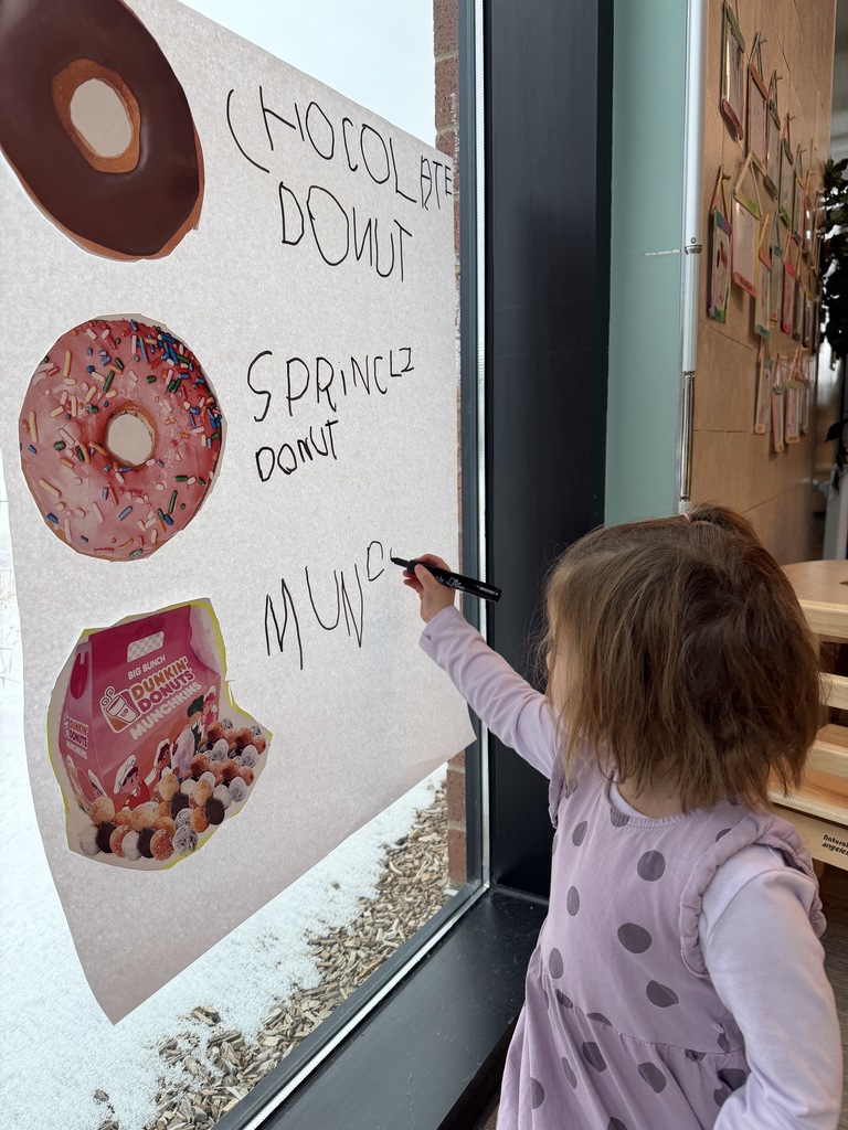 Student writing the name of the menu items on a larger poster.