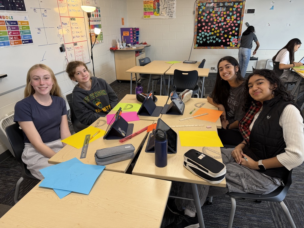 Four students sitting at a desk with paper and rulers.