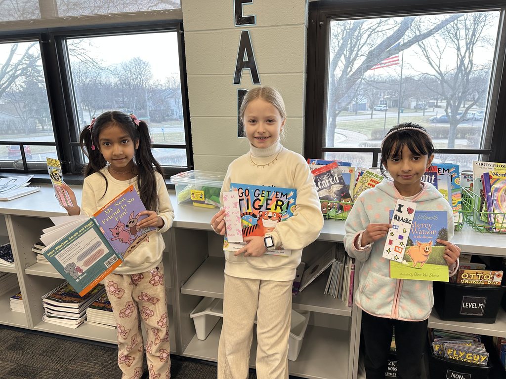 Three girls holding up a book and a bookmark.
