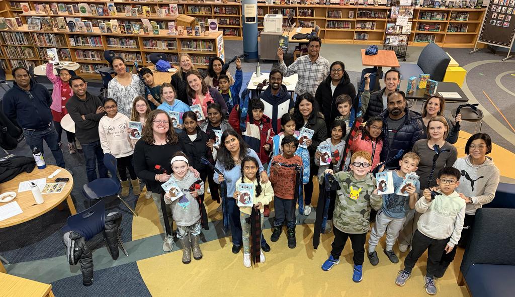 Group of students and parents standing with books at family reading night.