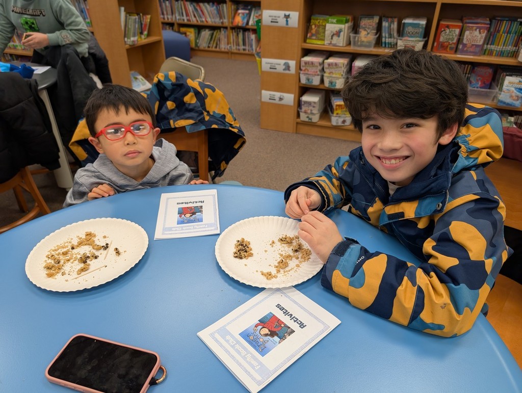 Two boys sitting at a table digging for bones on a plate.
