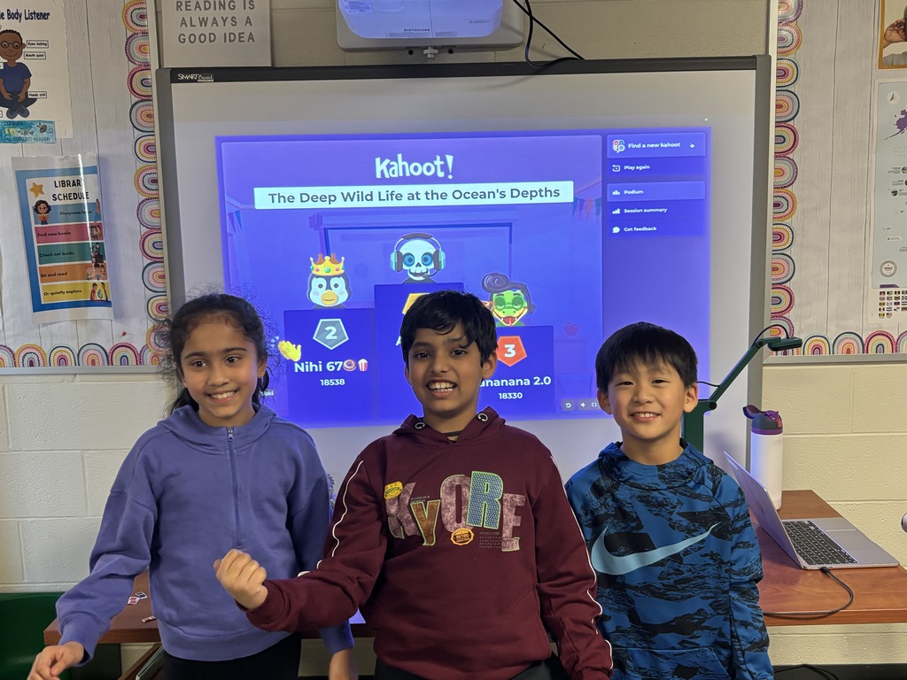 Students standing in front of the screen with their scores projected from the game.