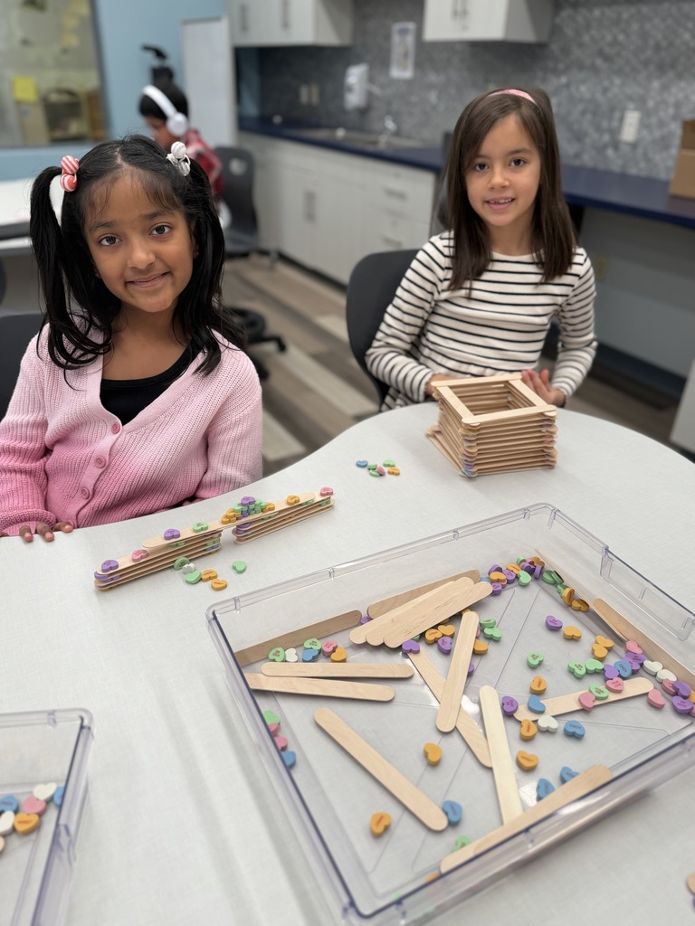 Students sitting at a table with activities and sticks to build with.