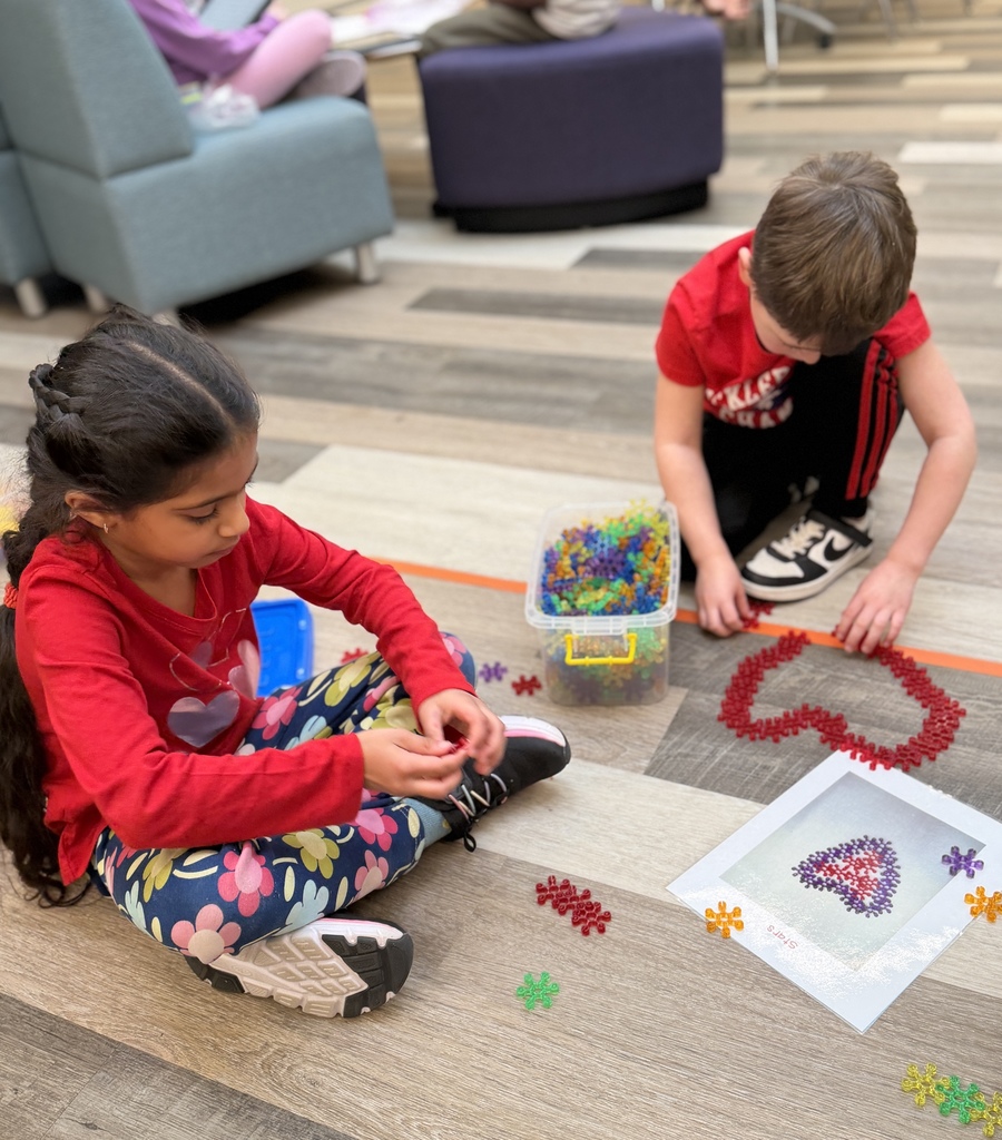 Students building hearts with STEM materials on the floor.