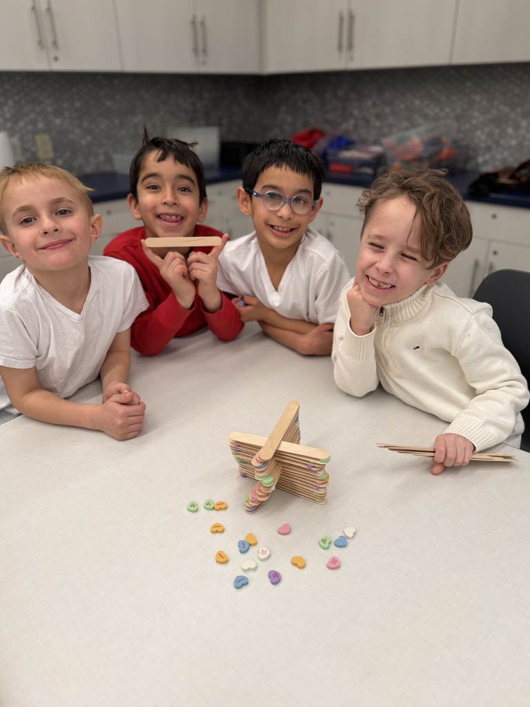 4 boys sitting at a table building towers with sticks and hearts