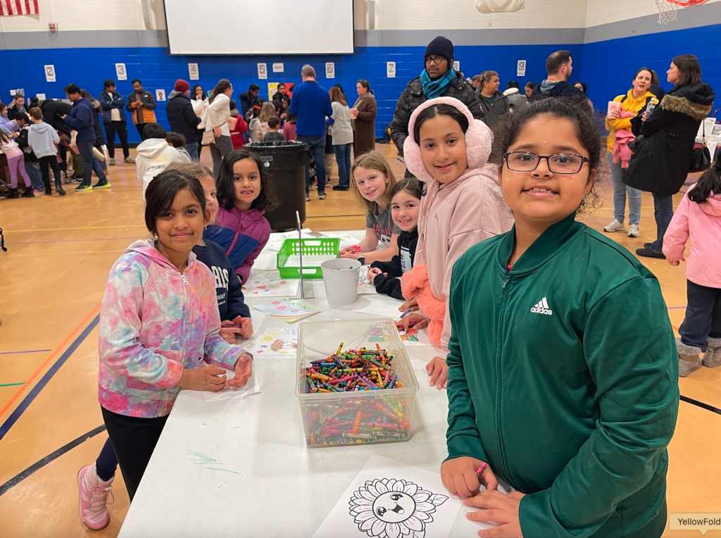Students standing at a table with crayons and coloring pages.