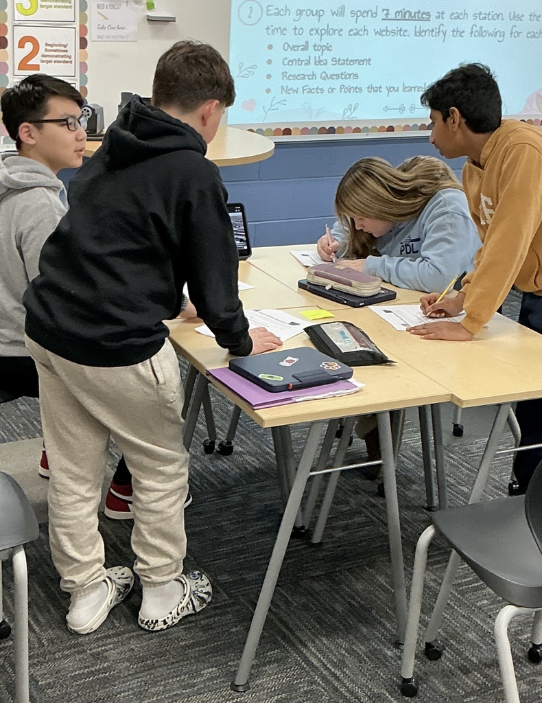 Students writing at their desks with a group of peers.