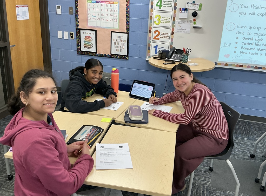 Students smiling at their desks with peers.