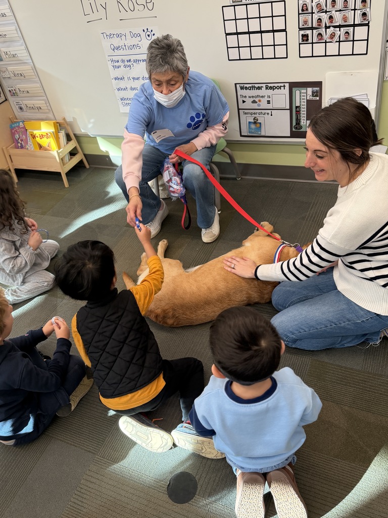 Dog owner is handing out rubber bracelets to kids, while the teacher pets the dog.