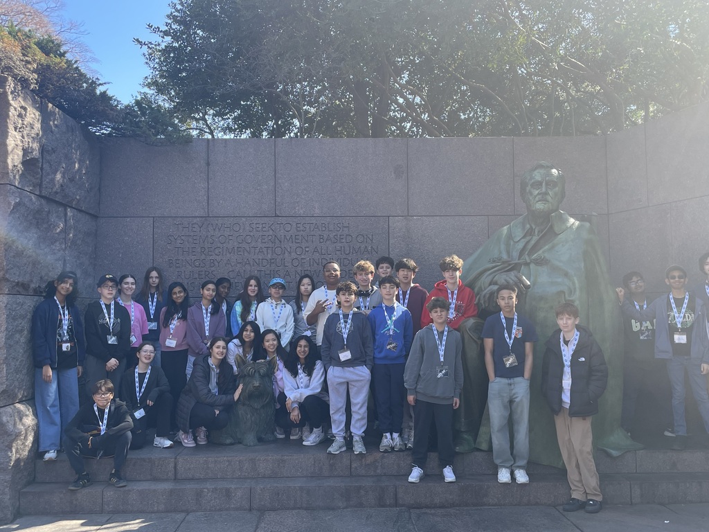A large group of students standing in front of a sculpture and memorial.