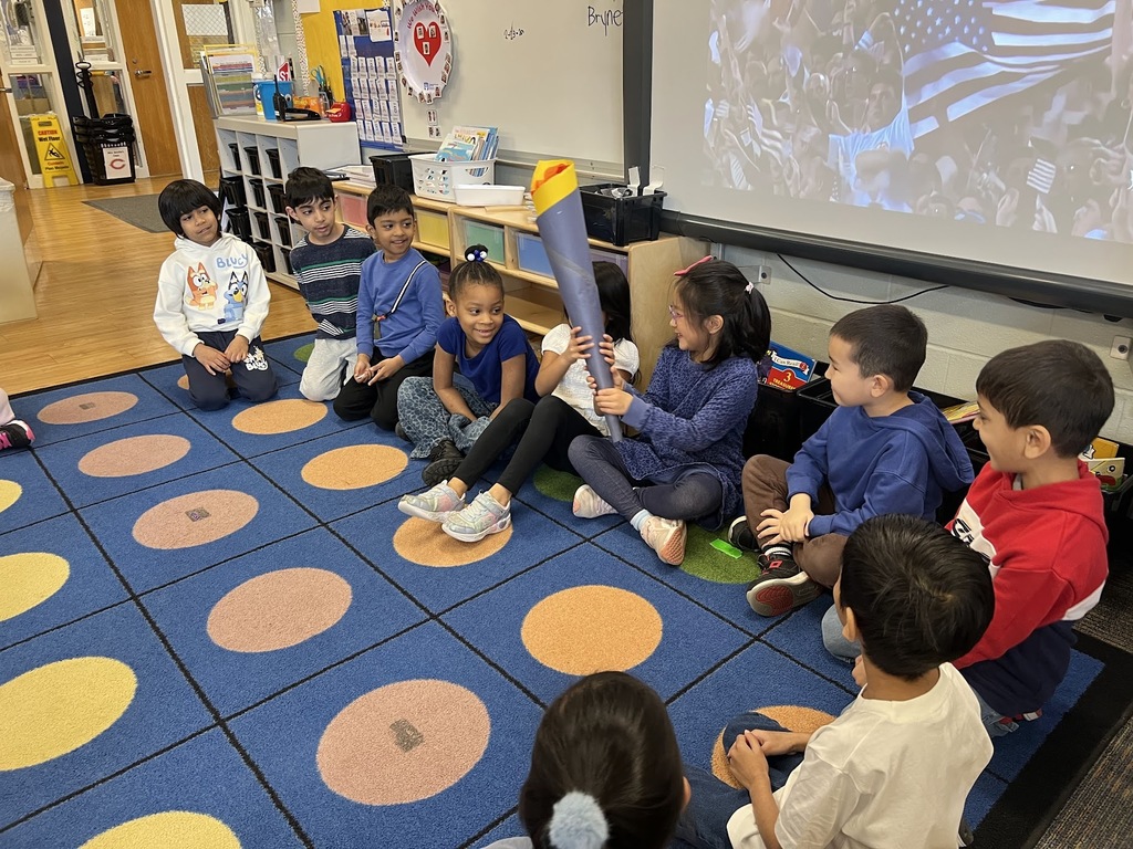 Students sitting in a circle on the rug passing a torch.