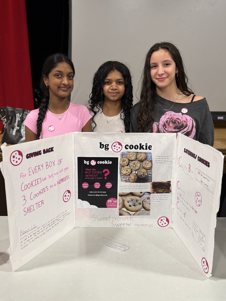 Three girls standing behind their project smiling for the photo. The poster board has cookies on it.